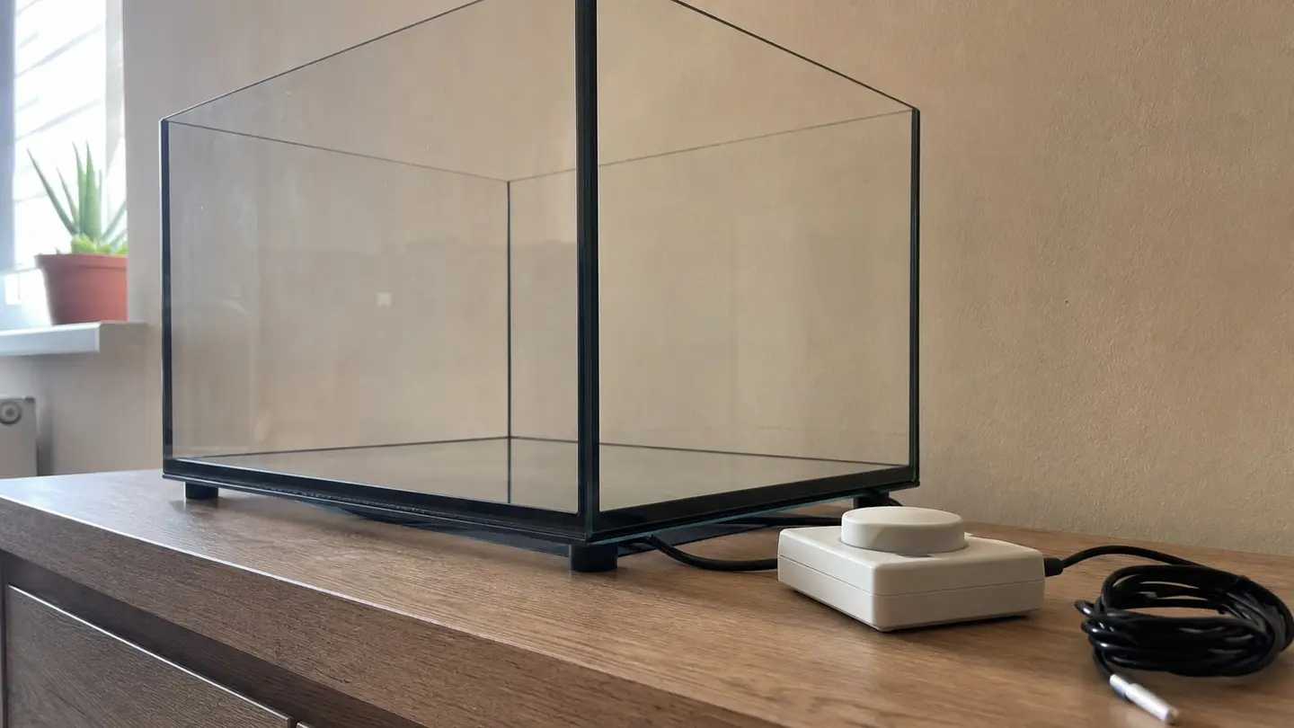 Puste szklane terrarium uniesione na podkładkach, pod dnem płaska mata grzewcza z przewodem, obok termostat z sondą